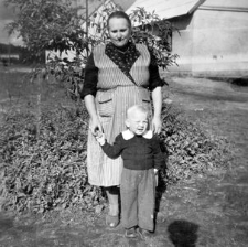 Maria Gliefe z wnukiem Janem na tle budynków mieszkalnych w Łupawie